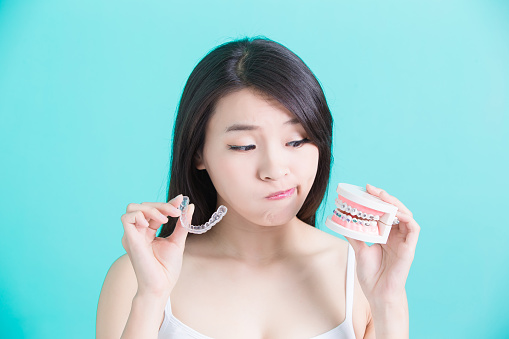 woman holding a model of teeth with braces in one hand and a clear aligner tray in the other hand and looking perplexed