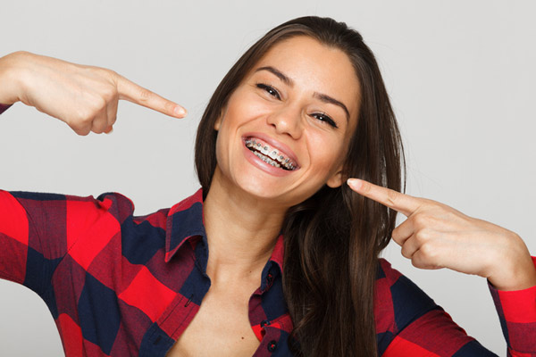 Woman with braces smiling and pointing at her mouth during the course of orthodontic treatment at Raleigh Family Orthodontics in Raleigh, NC