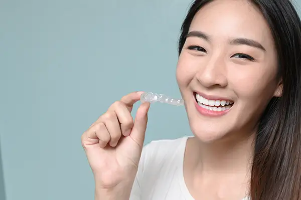 Young woman with a bright smile holding a clear aligner, promoting orthodontic solutions for adults.