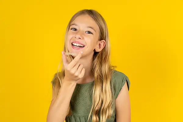 Happy blonde girl holding a clear aligner in her hand, showcasing dental alignment solutions for teens.