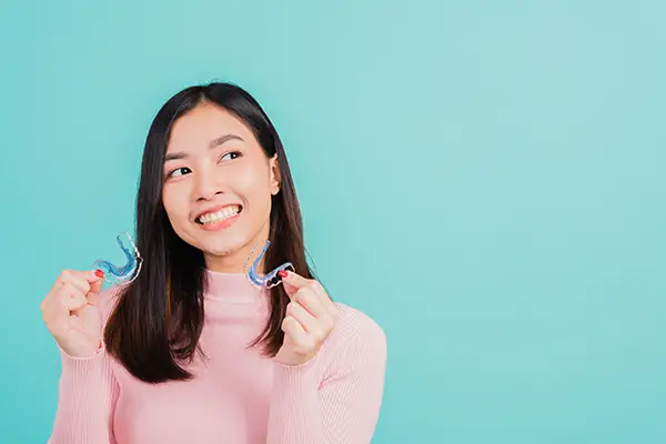 Young smiling woman holding clear retainers, encouraging their use after orthodontic treatment.