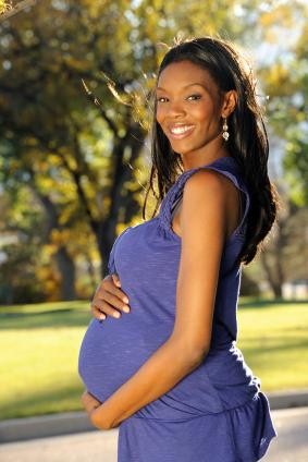 smiling pregnant black woman standing outside and holding her belly