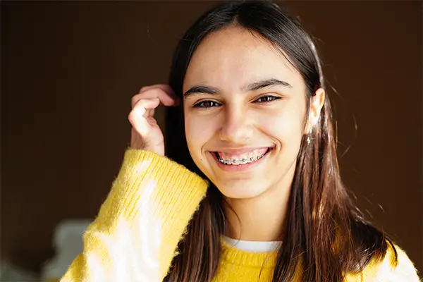 A teenage girl smiling confidently and showing her traditional metal braces.